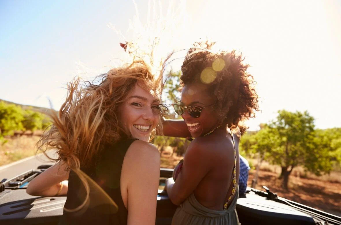 Duas mulheres sorriem em uma viagem de carro em um dia ensolarado