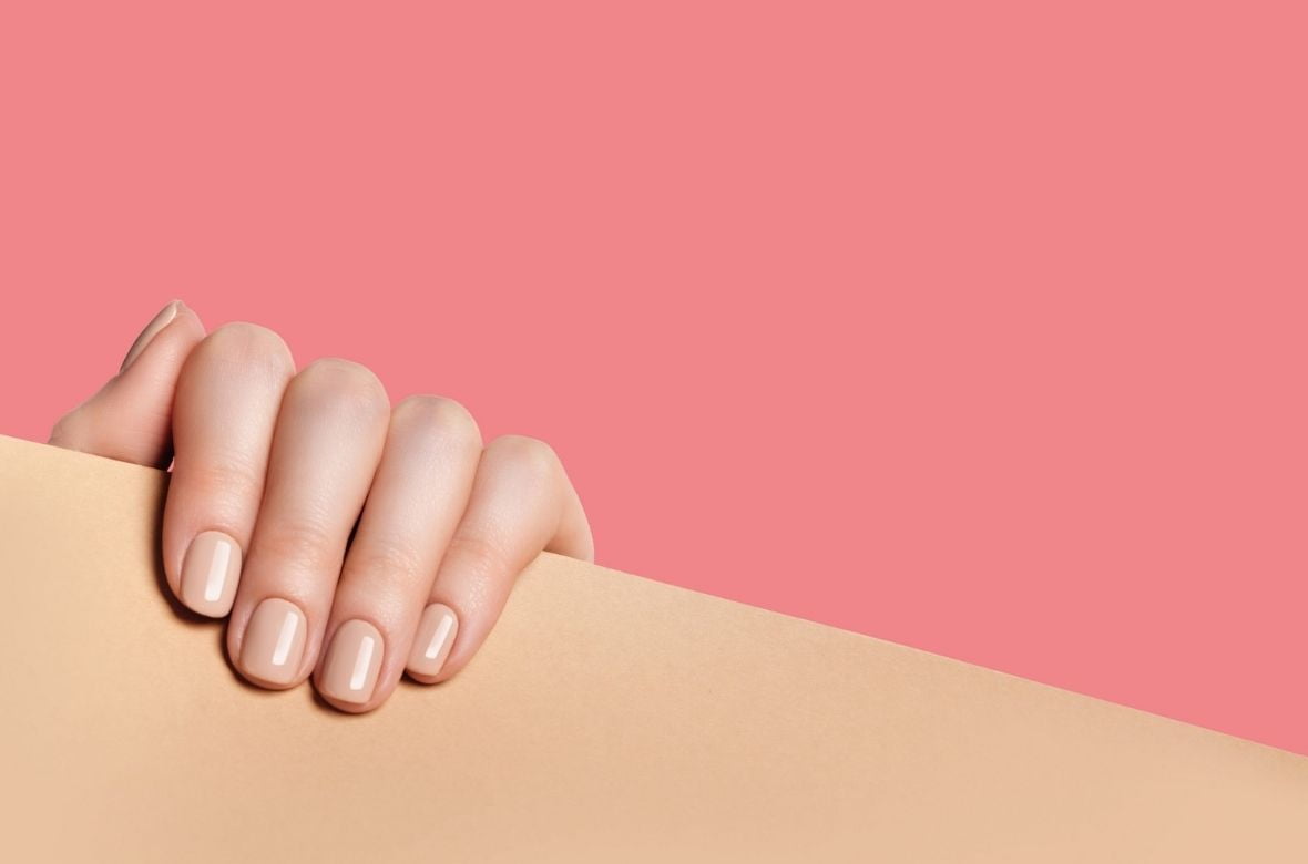Mão de mulher posicionada em um móvel de madeira realça suas unhas fortes e saudáveis